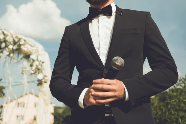 Formal wedding MC holding a handheld microphone outdoors