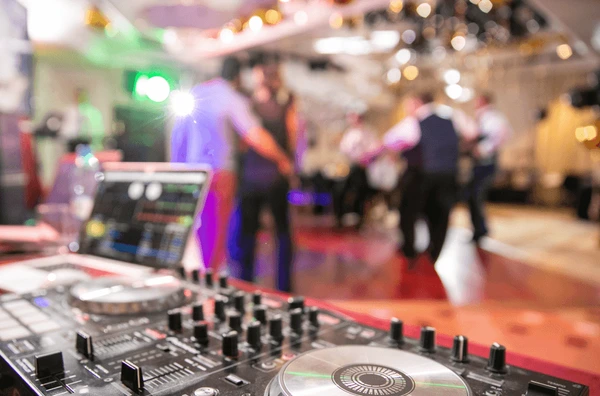 DJ mixer in the foreground with guests dancing at a reception