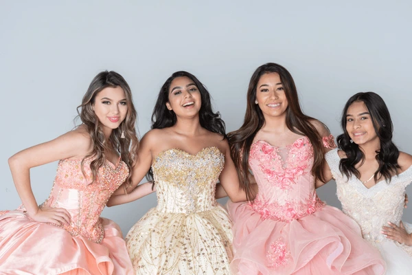 Four teenage girls posing together in pink and gold formal dresses