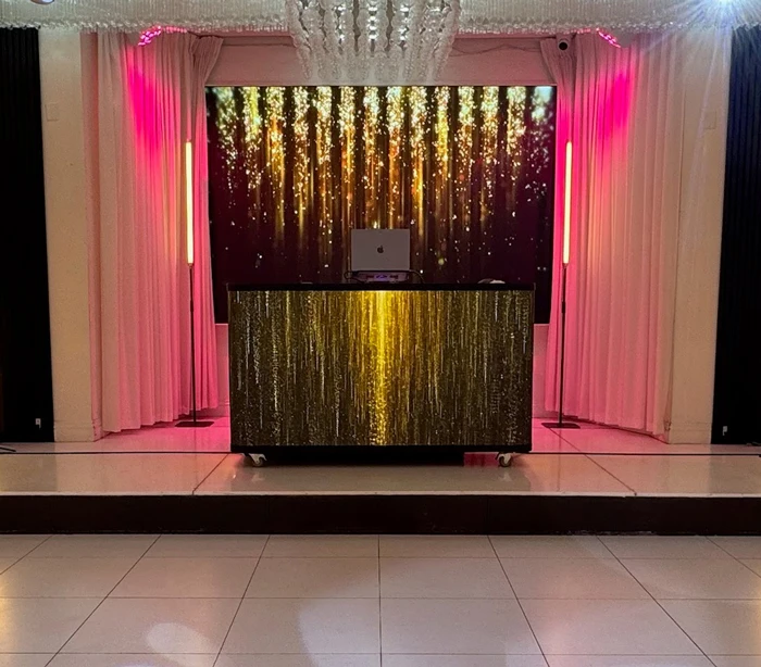 DJ booth in front of a large LED video wall with gold graphics and pink event lighting