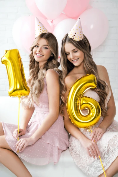 Two friends holding gold number 16 balloons at a pink birthday celebration