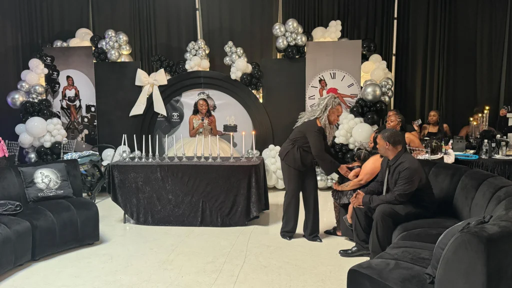 Sweet 16 honoree and family celebrating in front of a black, white and silver party backdrop