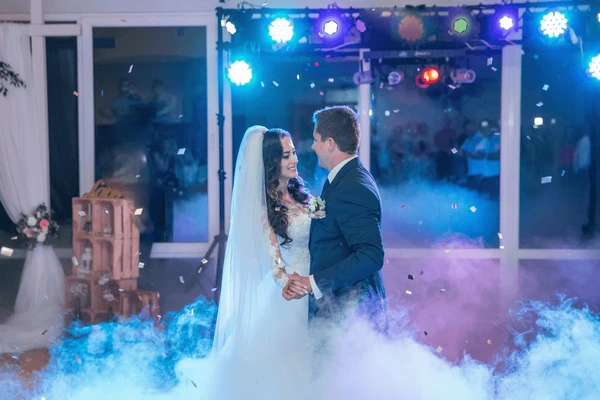 Bride and groom facing each other during a first dance with blue lighting and low fog