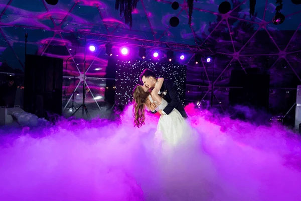Bride and groom kissing during their first dance under purple lighting and low fog