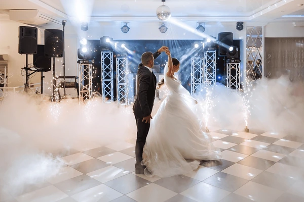 Bride and groom dancing on a checkered floor with DJ lighting, low fog and spark effects