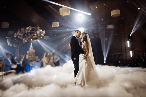 Bride and groom embracing under a spotlight while low fog covers the dance floor