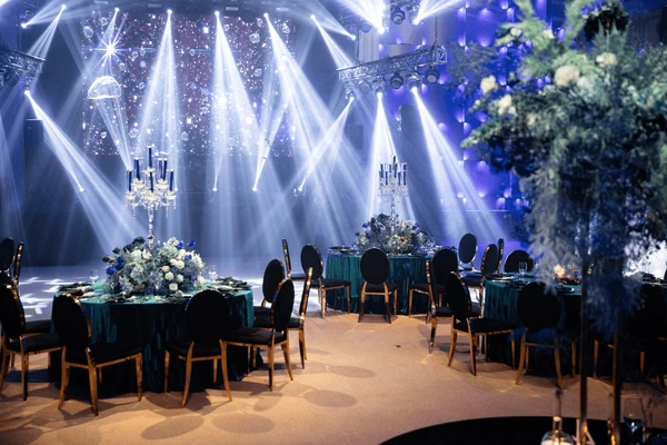Elegant wedding reception tables facing a stage illuminated with white beams of light